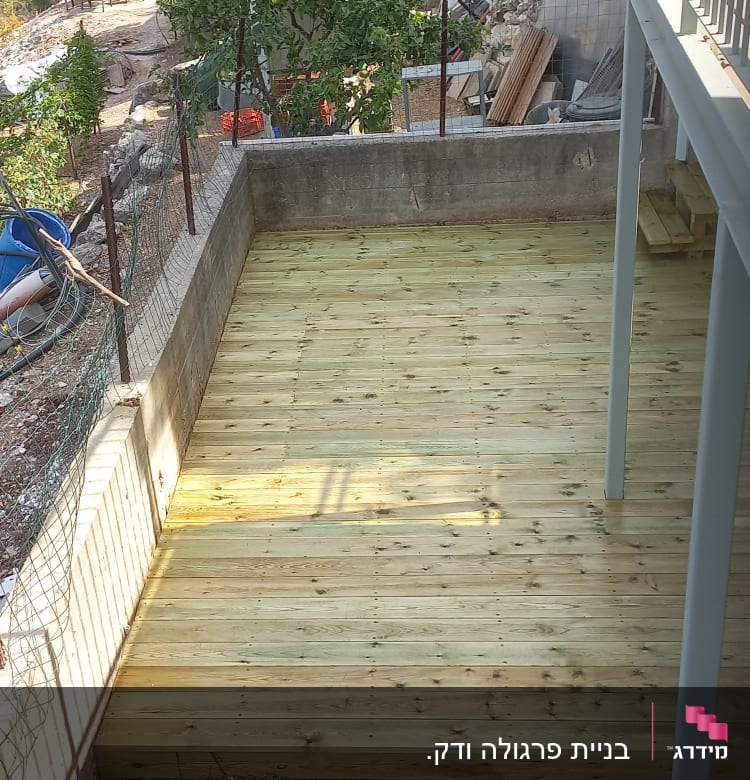 דק עץ חדש בגינה עם קיר בטון מסביב